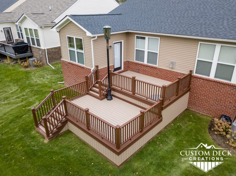 Two-tiered taupe and brown composite deck with stairs leading to backyard, and a street lamp on the deck