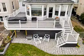 Aerial view of a two-level gray composite deck with white railings, attached to a house with a sunroom, featuring outdoor dining and stairs.